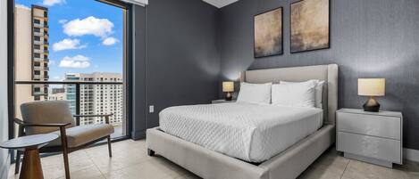 Een moderne slaapkamer met een groot bed, nachtkastjes, een stoel en een stadszicht door een groot raam.