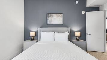 Un dormitorio moderno con una cama grande, dos mesitas de noche con lámparas, una pared de acento gris y una puerta.