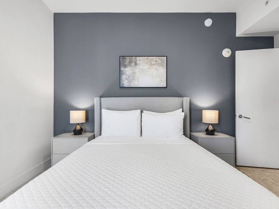 Un dormitorio moderno con una cama grande, dos mesitas de noche con lámparas, una pared de acento gris y una puerta.