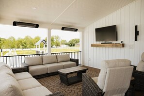 Eine überdachte Terrasse mit einer Couch, Stühlen, einem Couchtisch und einem an der Wand befestigten Fernseher.