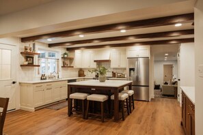 A modern kitchen with white cabinets, a central island with stools, a stainless steel refrigerator, and wooden beams on the ceiling. - Lux Family Retreat l Sauna + Hot Tub * Game Room~Swingset (Rising Sun)