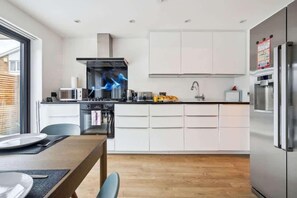 A modern kitchen with white cabinets, stainless steel appliances, and a dining area with a wooden table and chairs.