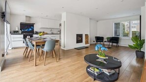 A modern kitchen with white cabinets, a flat-screen TV, and a dining area with a wooden table and chairs. - Contemporary 3-Bed House - Parking - By Tempstay (Windsor)