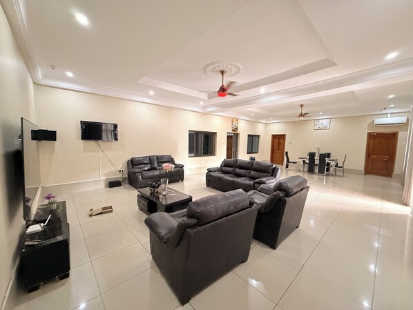 A spacious living room with two sofas, a coffee table, a TV, and a ceiling fan. - The best 5bedroom house with AC in a vibrant yet low key part of Accra. (Accra)