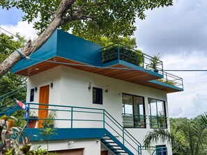 A two-story building with a blue and white exterior, wooden deck, and a staircase leading to the upper floor. - Serenity of Nature - Tiny Home in Manuel Antonio (Quepos)