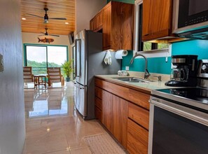 A modern kitchen with wooden cabinets, stainless steel appliances, and a view to the outside. - Serenity of Nature - Tiny Home in Manuel Antonio (Quepos)