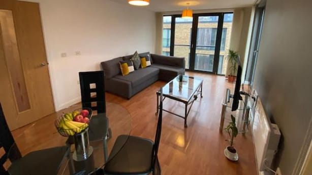 Una sala moderna con sofá, una mesa de centro de cristal y un comedor con sillas y una cesta de frutas.