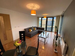 A modern living room with a sofa, a glass coffee table, and a dining area with chairs and a fruit basket. - Superb 1-bed Apartment in Birmingham City Centre (Birmingham)