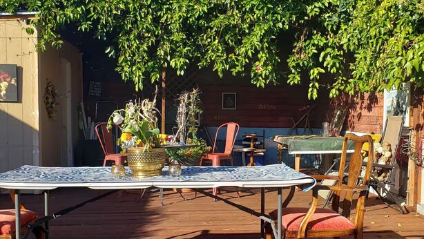 Un patio al aire libre con una mesa y sillas, rodeado de plantas en macetas y una terraza de madera.