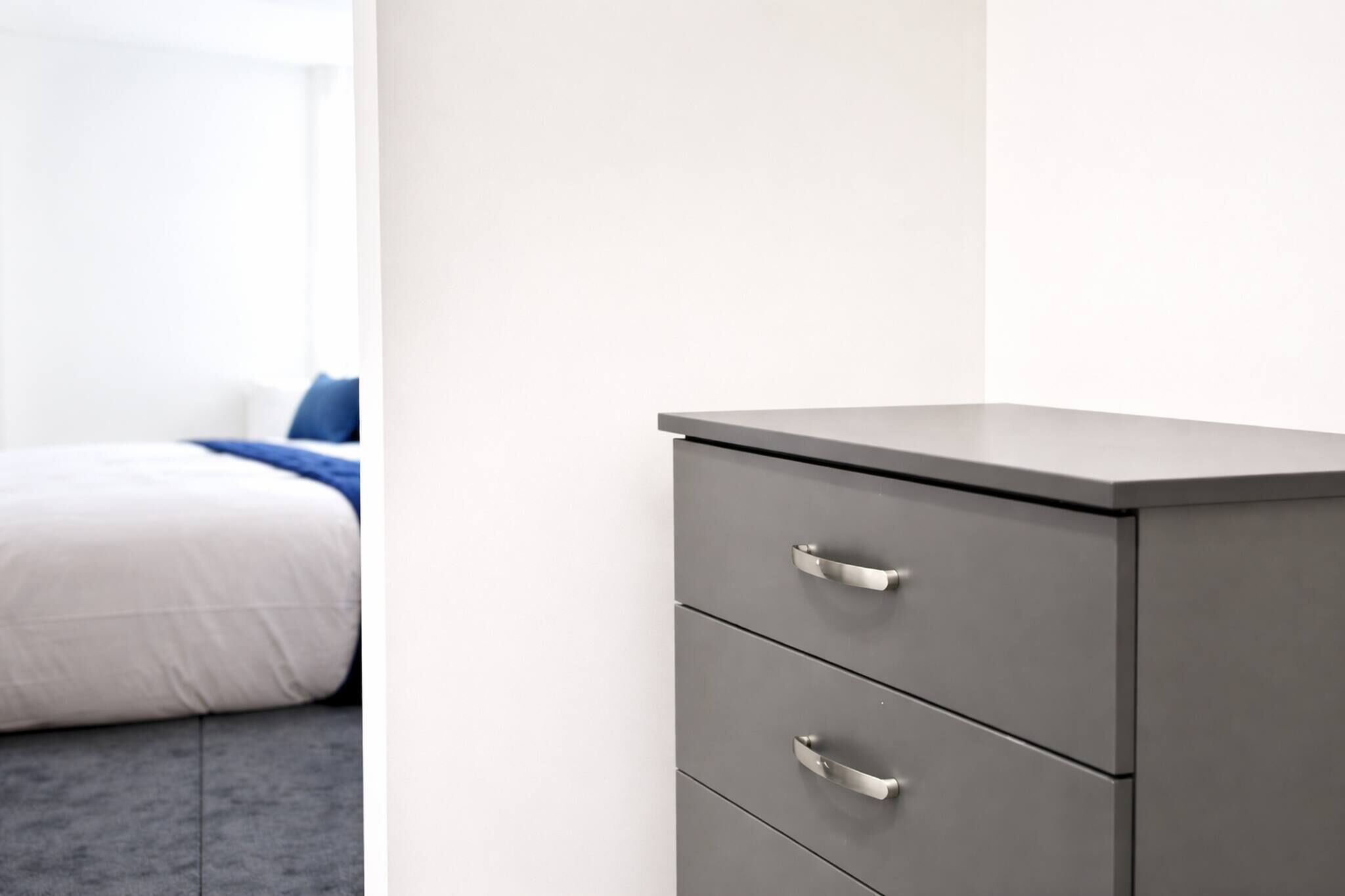 A modern bedroom with a bed, a grey filing cabinet, and a white wall.