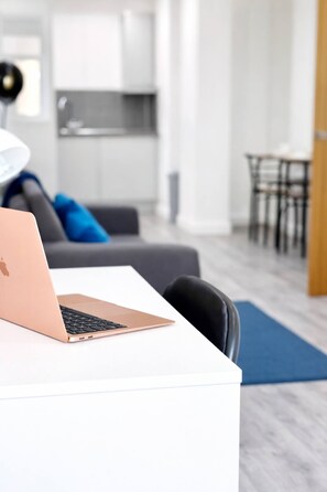 Een moderne woonkamer met een witte bank, een laptop op een witte tafel, en een eethoek op de achtergrond.