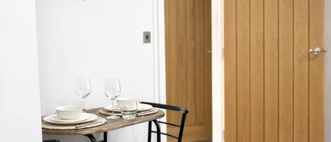 A dining area with a wooden table set for two, a metal chair, and a wooden door in the background.