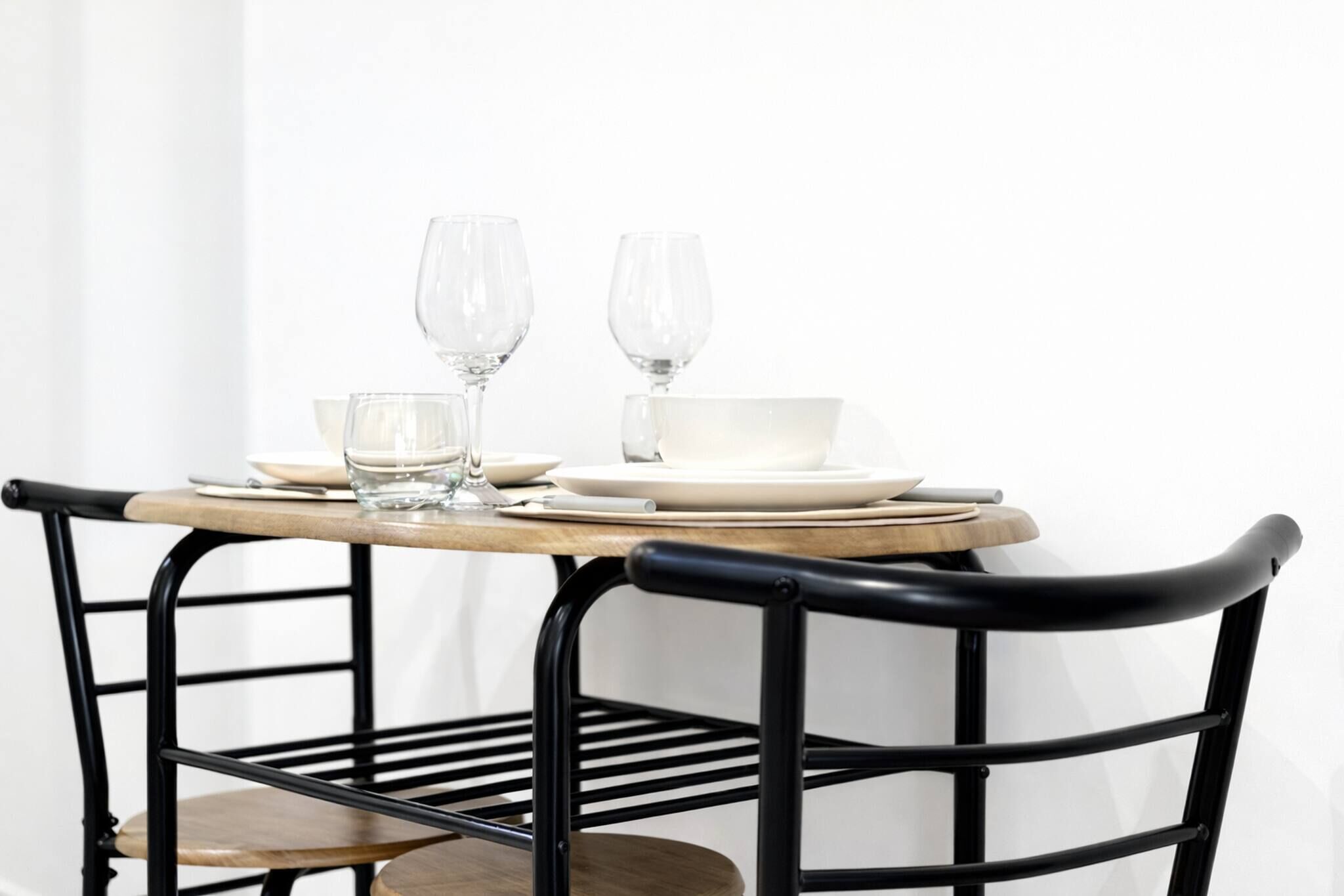 A table with two wine glasses, a bowl, and plates set on a wooden table with a metal frame.