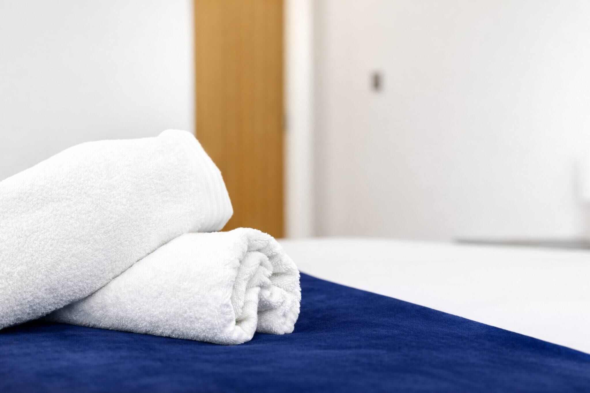 Une serviette blanche, soigneusement pliée, est posée sur un couvre-lit bleu dans une chambre d’hôtel.