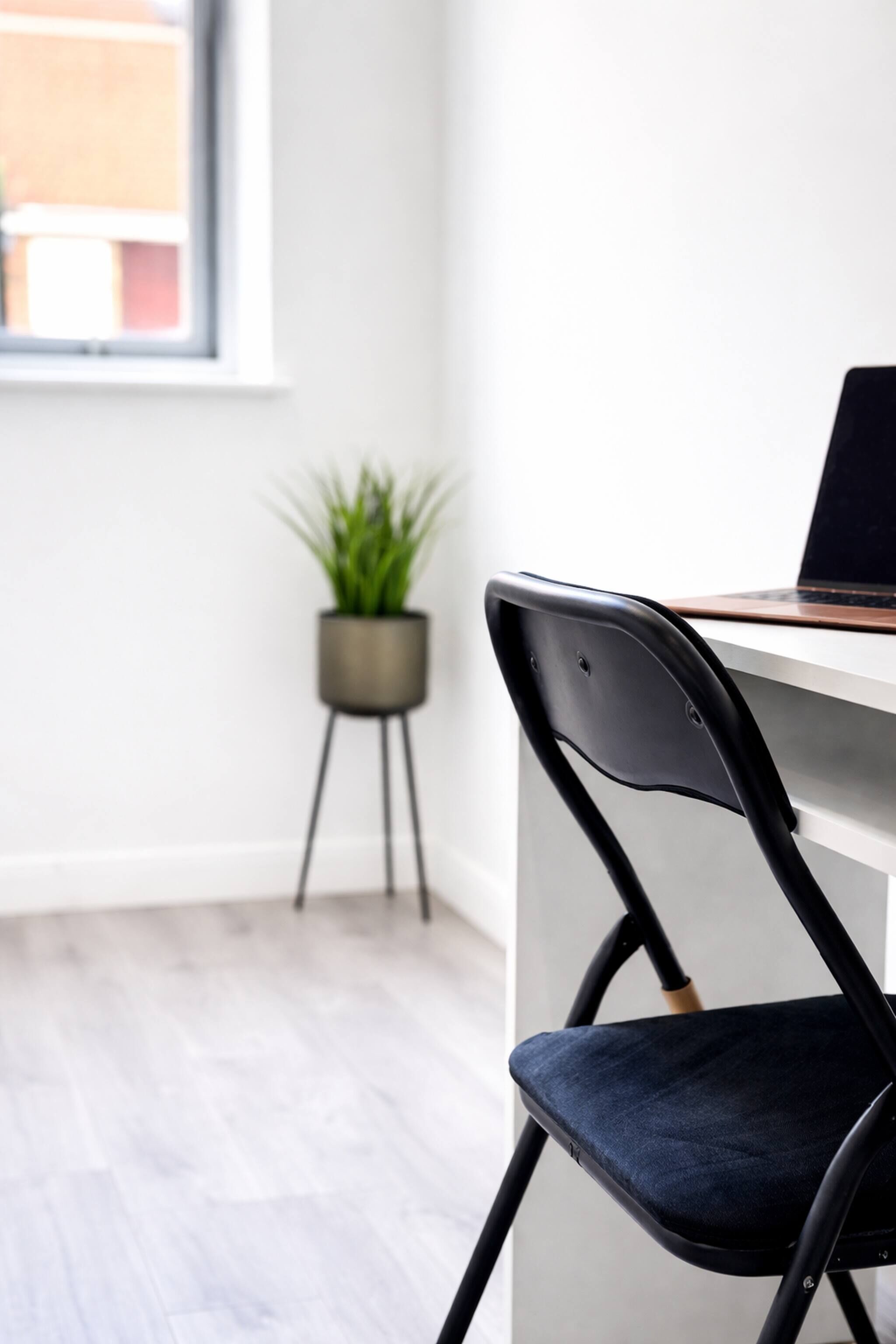 Une chaise de bureau moderne avec un coussin foncé, un ordinateur portable posé sur un bureau et une plante en pot en arrière-plan.