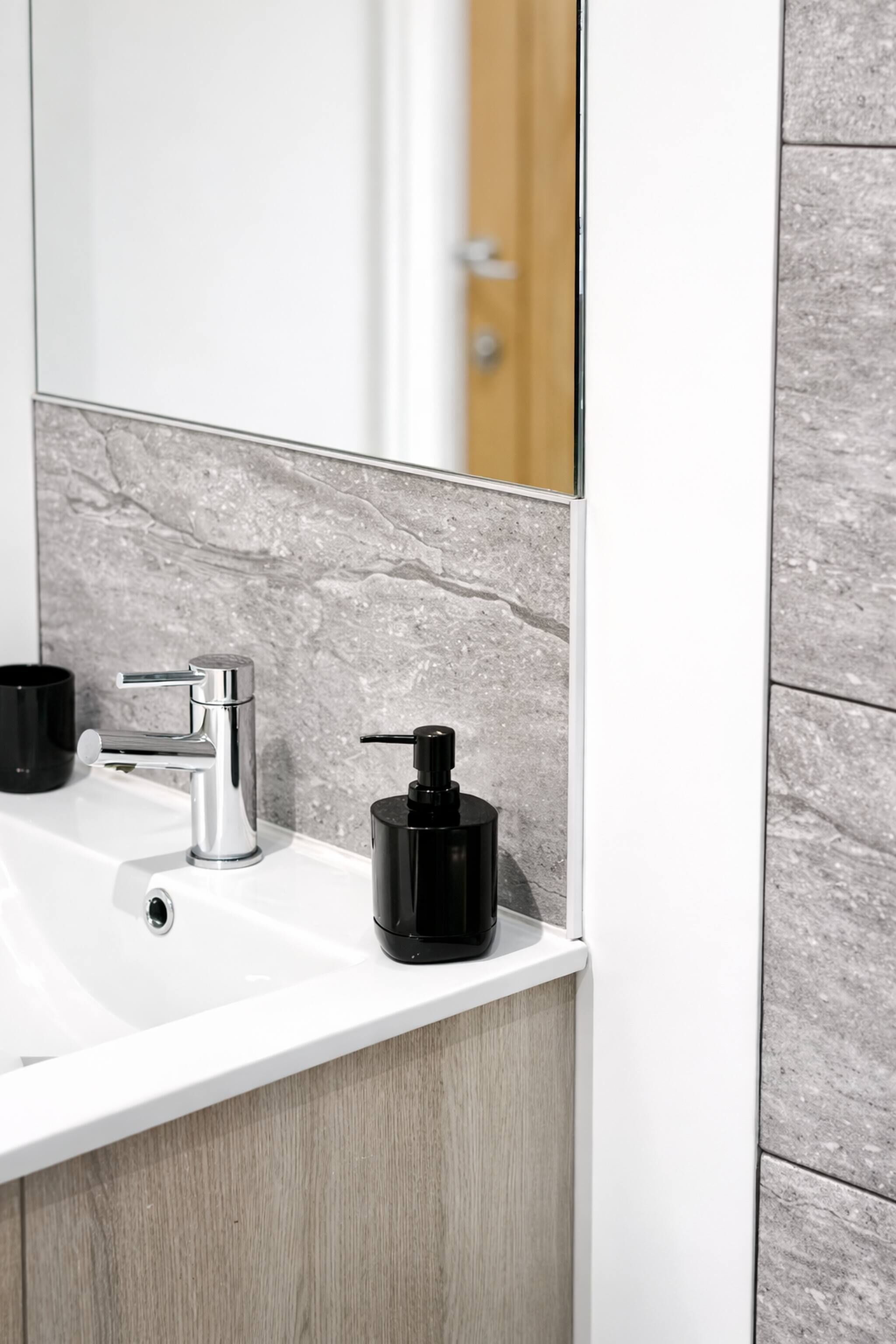 A bathroom with a white sink, a chrome faucet, and a black soap dispenser.
