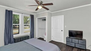 Une chambre à coucher avec un lit, un ventilateur de plafond, une télévision, une commode et un placard.