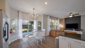 A modern kitchen with a built-in TV, white cabinets, and a dining area with a table and chairs. - WH7712 - 6BR house w/ Resort Access near Disney (Kissimmee)