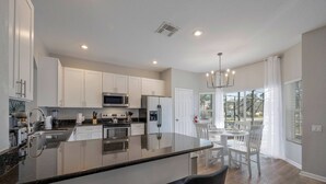 A modern kitchen with white cabinets, stainless steel appliances, and a central island with bar seating. - WH7712 - 6BR house w/ Resort Access near Disney (Kissimmee)