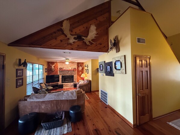 Un salon chaleureux avec une cheminée, des poutres apparentes en bois au plafond et un manteau de cheminée en pierre.