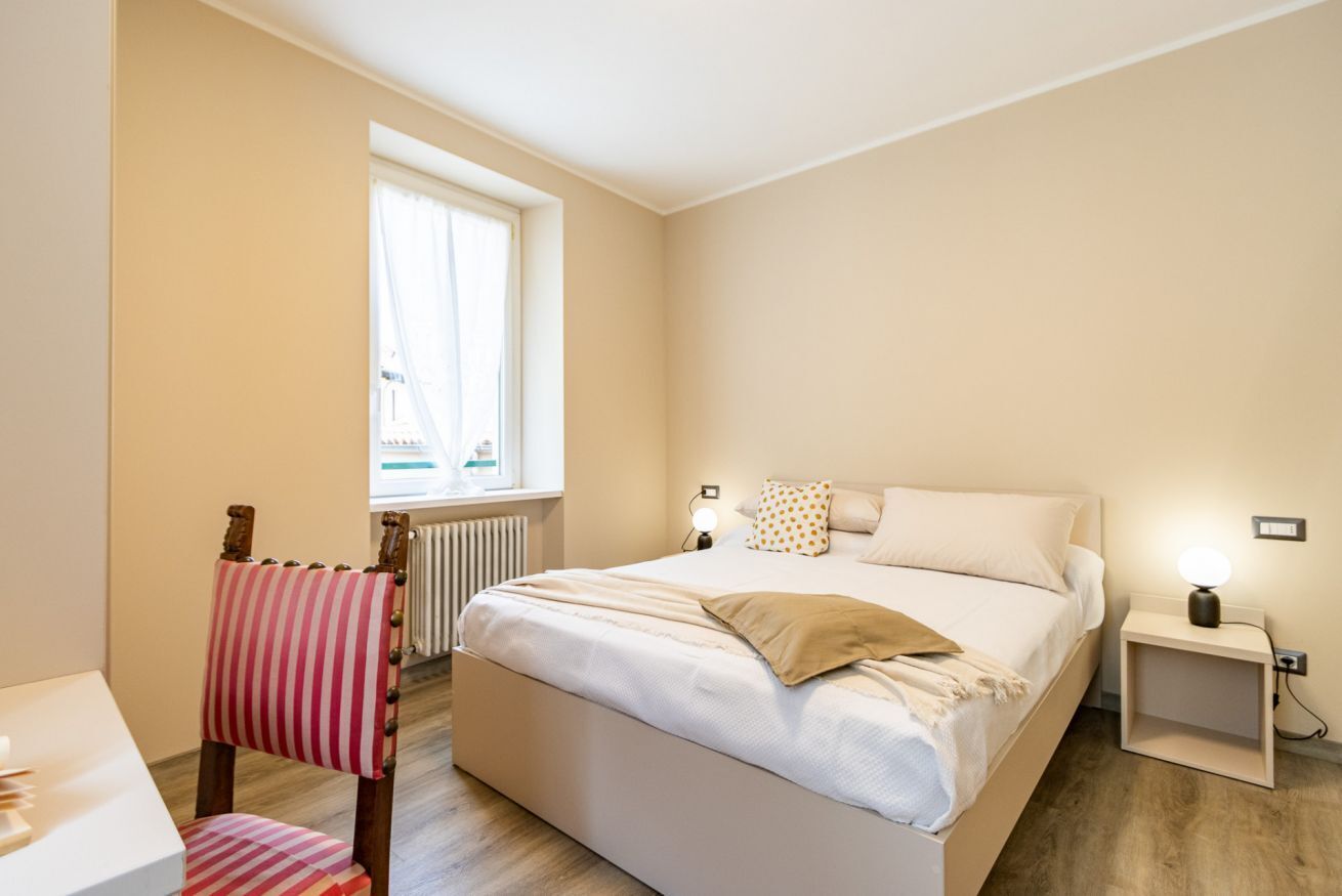 Une chambre à coucher avec un lit, des tables de chevet, une fenêtre, un radiateur et une chaise.