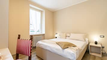 Une chambre à coucher avec un lit, des tables de chevet, une fenêtre, un radiateur et une chaise.