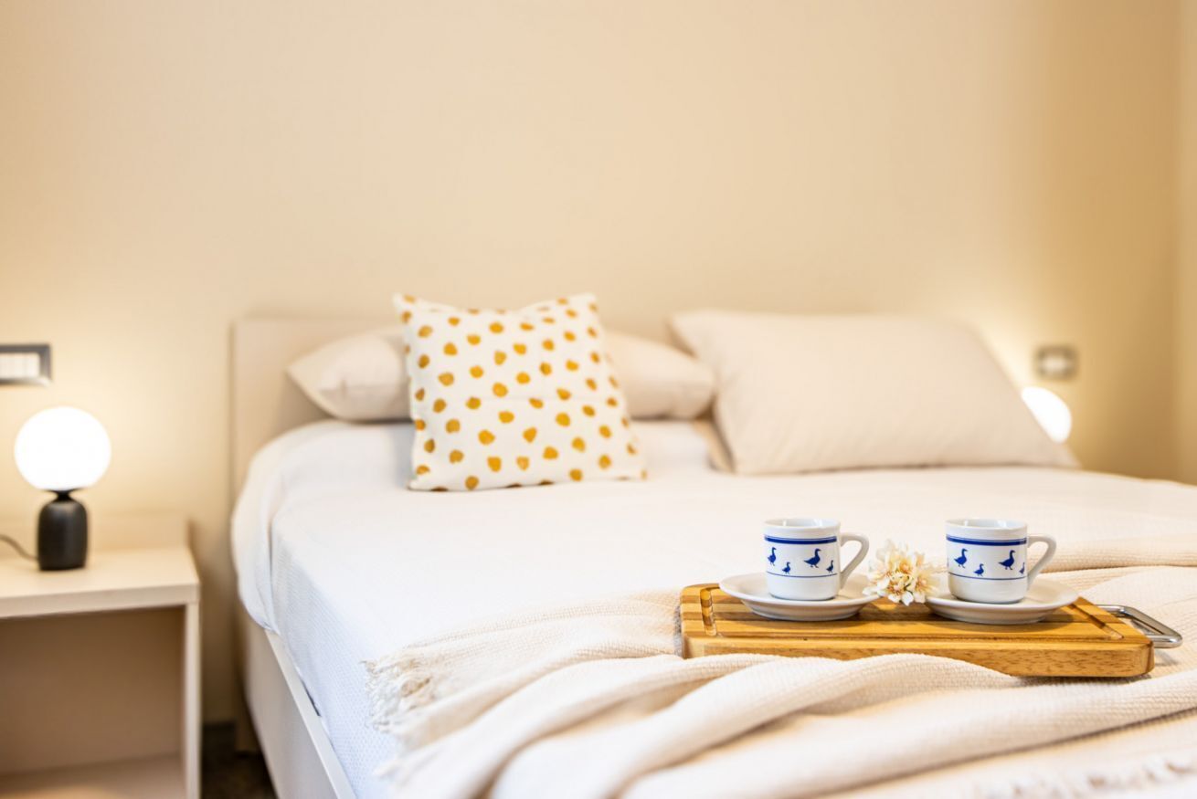 Un lit bien fait, agrémenté d’un coussin blanc à pois dorés, d’une lampe de chevet et d’un plateau sur lequel reposent deux tasses et leurs soucoupes.