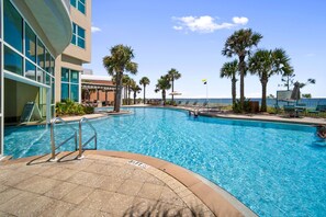 A pool area with a clear view of the ocean, surrounded by palm trees and lounge chairs. - Luxury Beachfront 3 Bedroom @ Aqua Resort, Walk to Pier Park and Topgolf & More! (Panama City Beach)