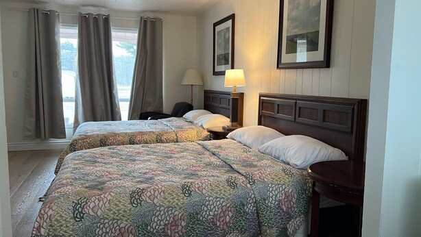 A hotel room with two beds, a nightstand, a lamp, a chair, and a window with curtains. - Seeleys Bay Motel and Resort (Seeleys Bay)