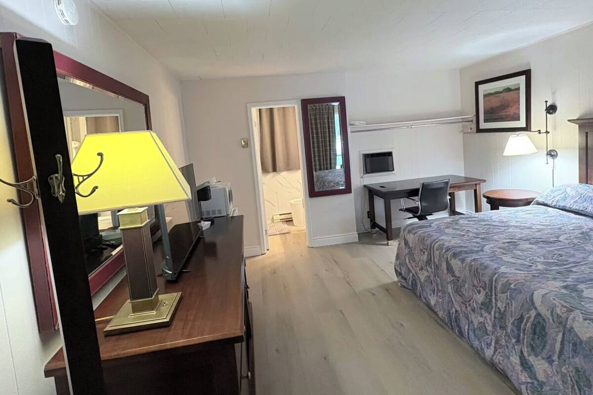 A hotel room with a bed, desk, chair, lamp, and a mirror.