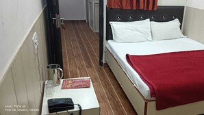 A narrow room with a bed, a small table with a telephone, and a wall-mounted light fixture. - Hotel Silsila (Varanasi)