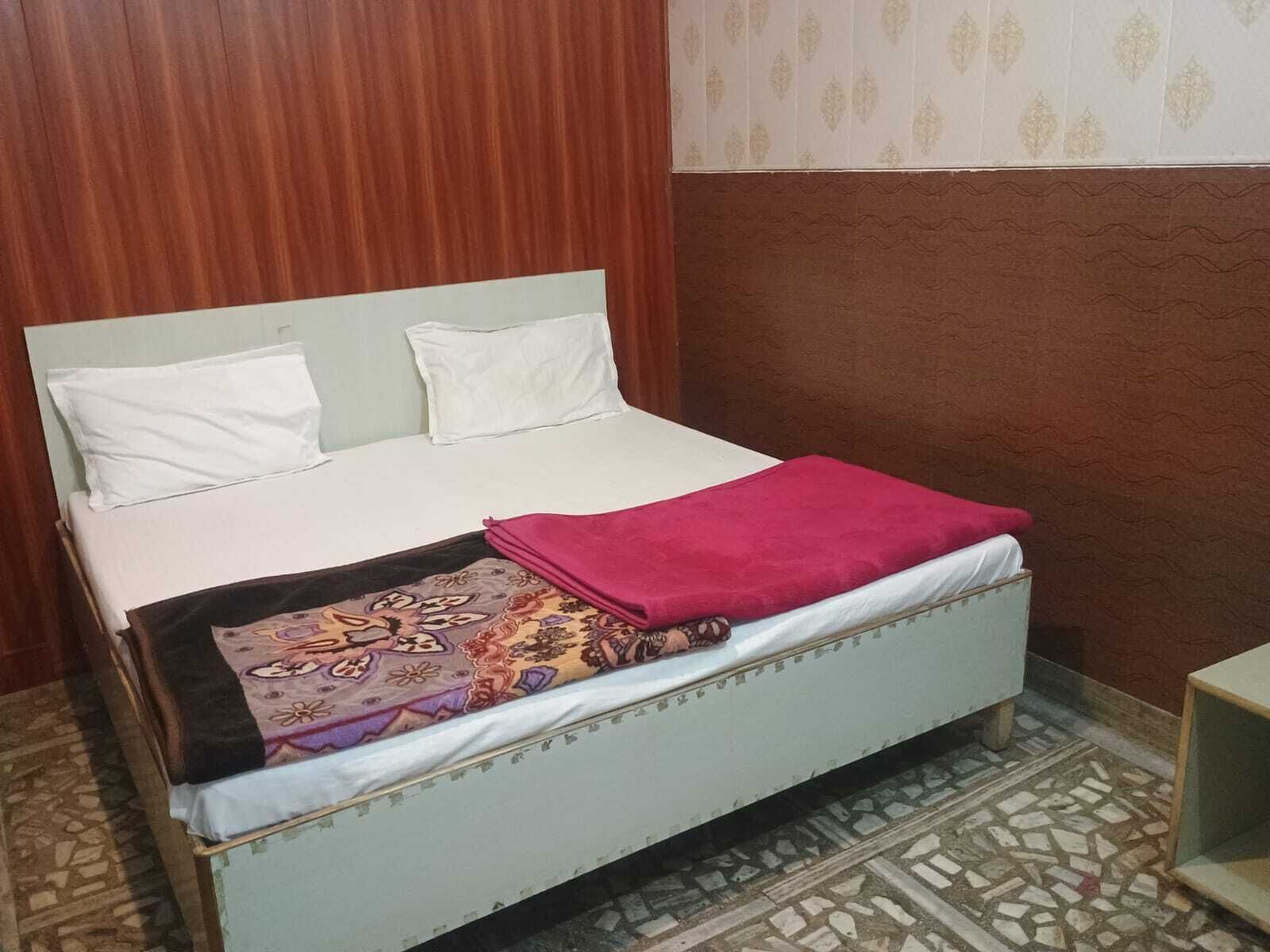 Un lit avec une literie blanche et une couverture colorée, une tête de lit en bois et un mur orné de motifs.