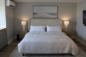 Un dormitorio con una cama grande, dos mesitas de noche con lámparas, aire acondicionado de pared y un cuadro sobre la cama.