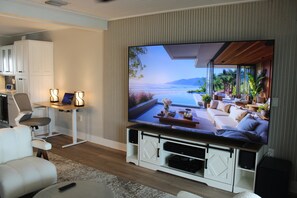 A modern living room with a large flat-screen TV, comfortable seating, a small table with two lamps, and a kitchen area in the background. - Waterfront 3-bedroom townhome on Island Estates, Clearwater Beach (Clearwater)