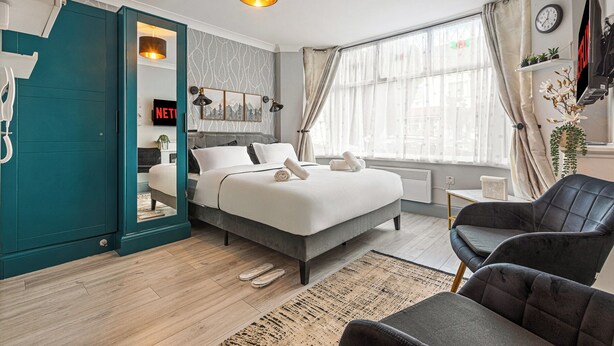 Un dormitorio moderno con cama, una silla, escritorio y ventana.