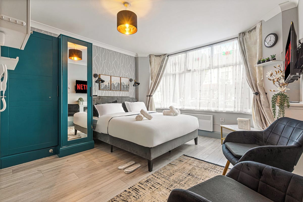 A modern bedroom with a bed, a chair, a desk, and a window.