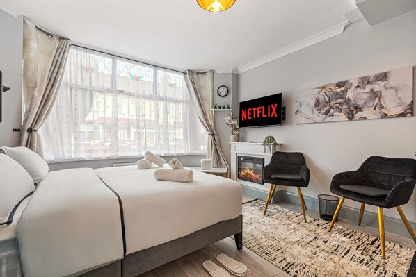 A modern bedroom with a bed, a fireplace, a TV, and a view of the outside. - Imperial Inn Apartments (London)
