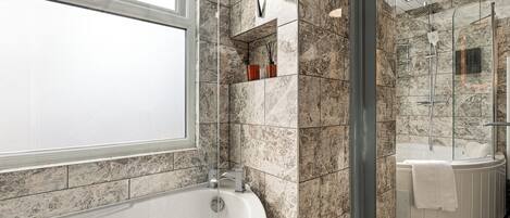 A modern bathroom with a freestanding bathtub, a glass shower enclosure, and a marble-tiled wall.