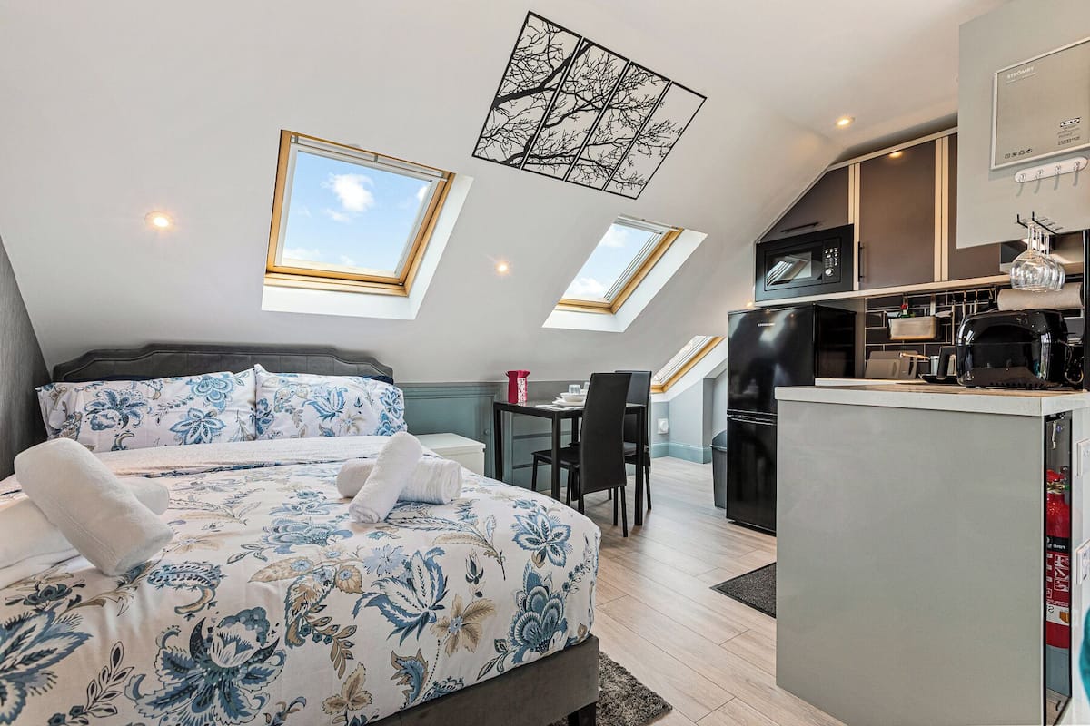 A bedroom with a bed, a desk, and a kitchenette.