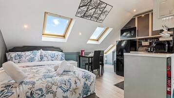A bedroom with a bed, a desk, and a kitchenette.