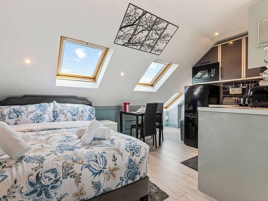 A bedroom with a bed, a desk, and a kitchenette.