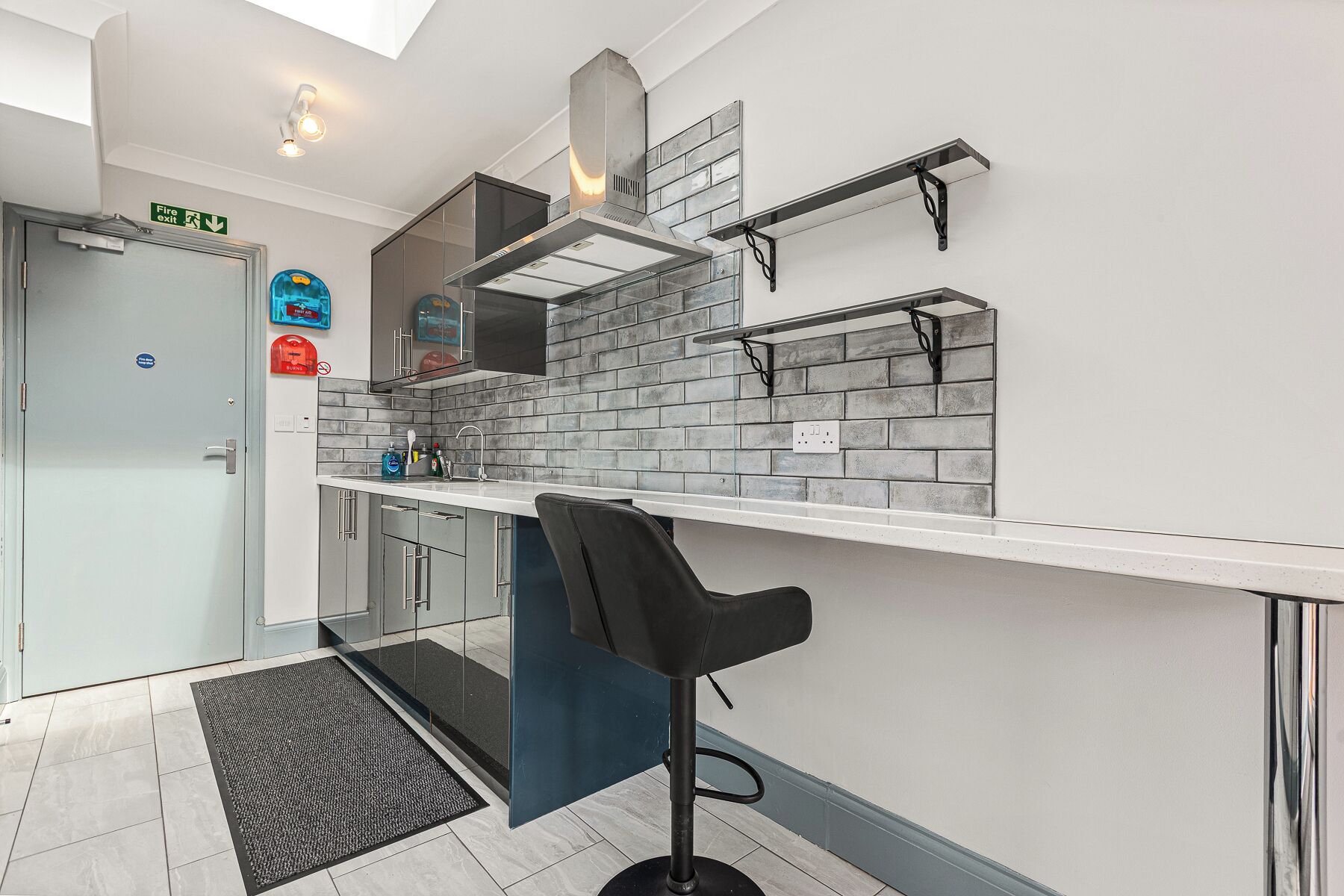 A modern kitchen with a white countertop, a black bar stool, and a fire exit sign.