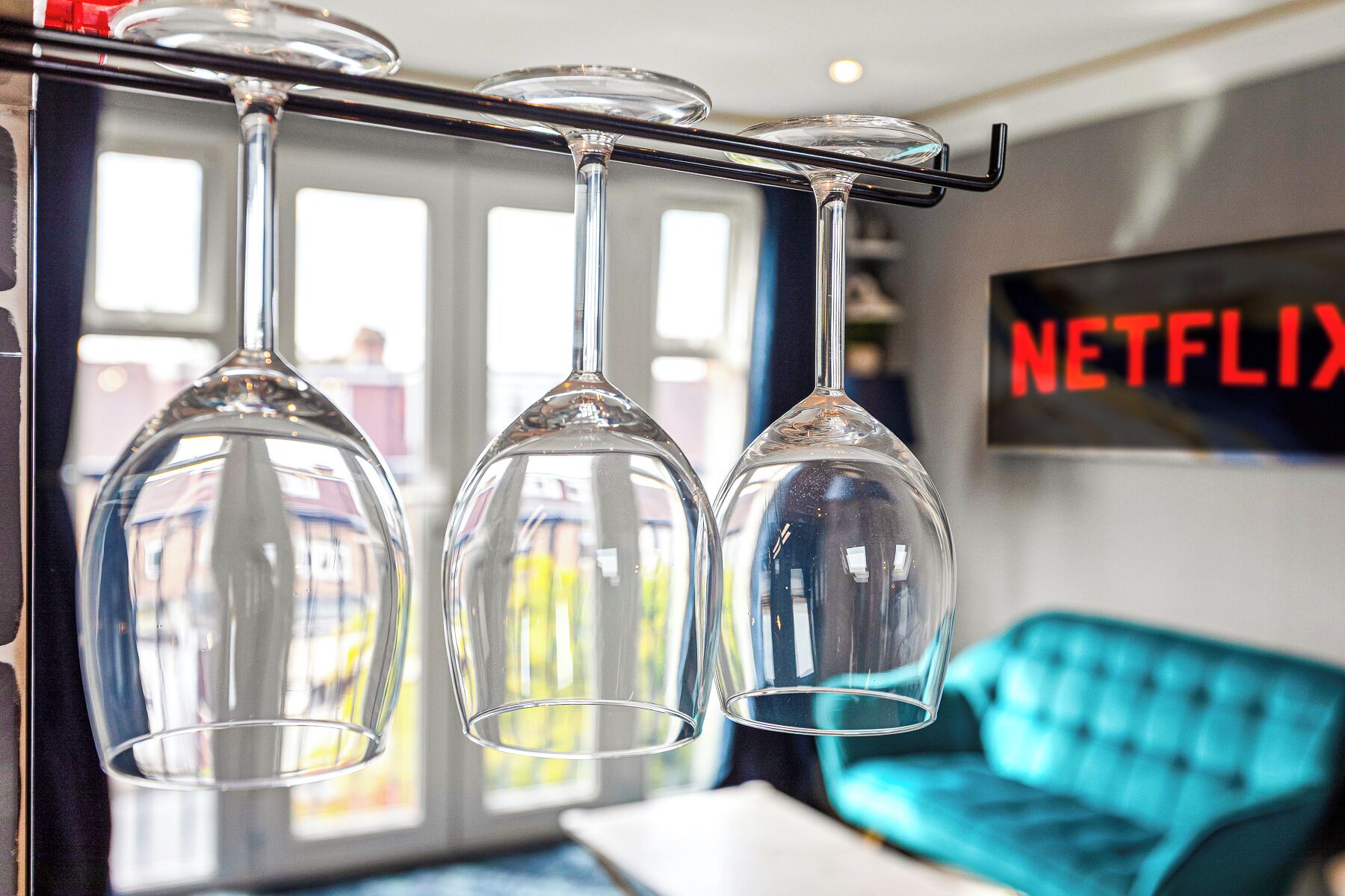 Three wine glasses hanging from a bar, a blue sofa, and a wall-mounted sign with the word "NETFLIX".