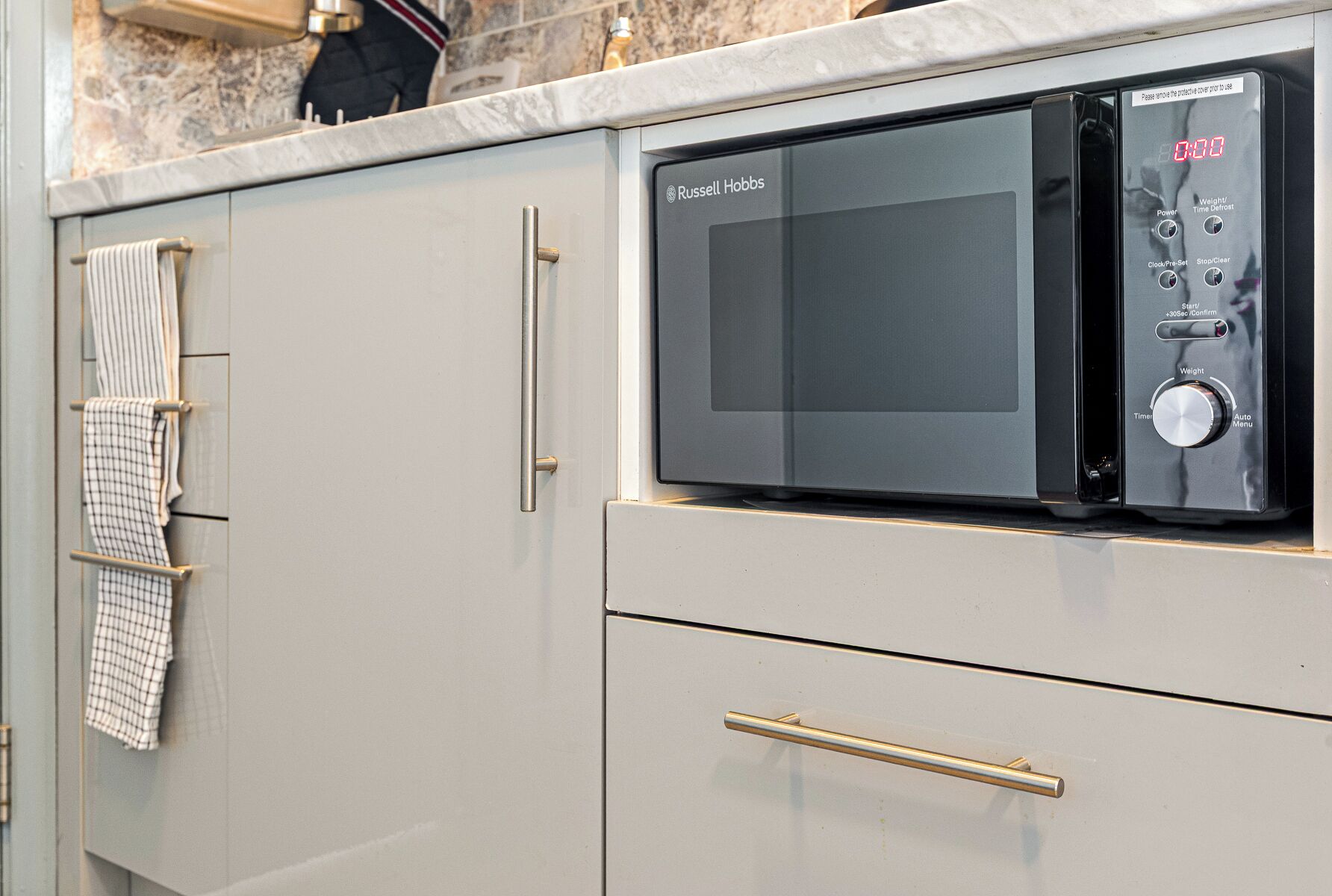 Een keuken met een ingebouwde magnetron, een handdoekhouder en een kast met een lade.