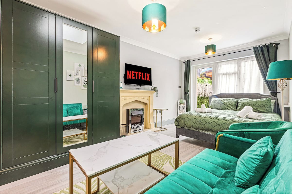 A modern bedroom with a green sofa, a bed with green bedding, a fireplace, and a TV displaying 'NETFLIX'.