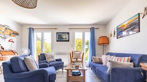 A living room with two blue sofas, a wooden coffee table, a wicker chair, a fan, and a lamp.