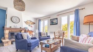 A living room with a fireplace, blue sofas, a coffee table, and a large window with curtains.