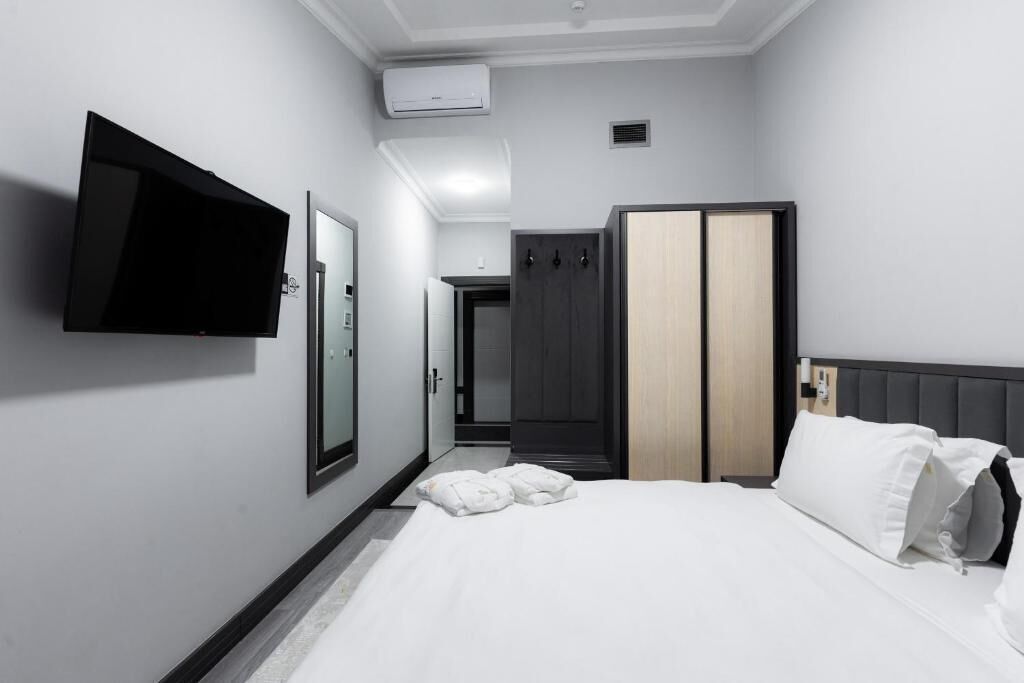 A hotel room with a bed, a flat-screen TV mounted on the wall, a wardrobe, and a door leading to a bathroom.