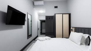 A hotel room with a bed, a flat-screen TV mounted on the wall, a wardrobe, and a door leading to a bathroom.