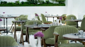 A dining area with green upholstered chairs, wooden tables, and white vases with purple flowers. - Rauza Hotel Tashkent (Tashkent)
